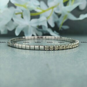 K&ouml;nnte beinhalten: Ein silbernes Armband mit einer Reihe kleiner Diamanten, die in einem wei&szlig;en Metallband gefasst sind. Das Armband besteht aus quadratischen Gliedern.