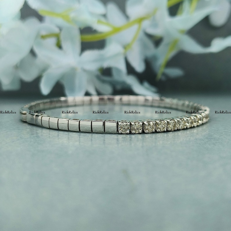 K&ouml;nnte beinhalten: Ein silbernes Armband mit einer Reihe kleiner Diamanten, die in einem wei&szlig;en Metallband gefasst sind. Das Armband besteht aus quadratischen Gliedern.