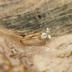 May include: A gold ring with a large, rectangular, clear gemstone and two smaller pear-shaped gemstones. The ring is set on a wooden surface, showcasing the ring's design and sparkle.