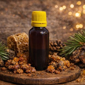 May include: A brown glass bottle with a yellow cap sits on a wooden surface, surrounded by pine needles, tree bark, and amber-colored resin. The background features a blurred bokeh effect.