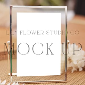 Może przedstawiać: Srebrna ramka do zdjęć z białym tłem i tekstem "LILY FLOWER STUDIO CO MOCK UP" na plecionym tacy z białymi kwiatami.