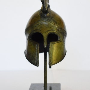 May include: A bronze replica of a Greek warrior helmet with a plume on top, displayed on a black marble base.