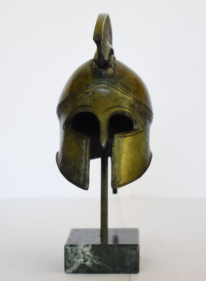 May include: A bronze replica of a Greek warrior helmet with a plume on top, displayed on a black marble base.