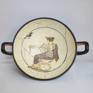 May include: A black and white ceramic bowl with a black bird and a woman playing a lyre. The bowl has a cracked glaze and two handles.