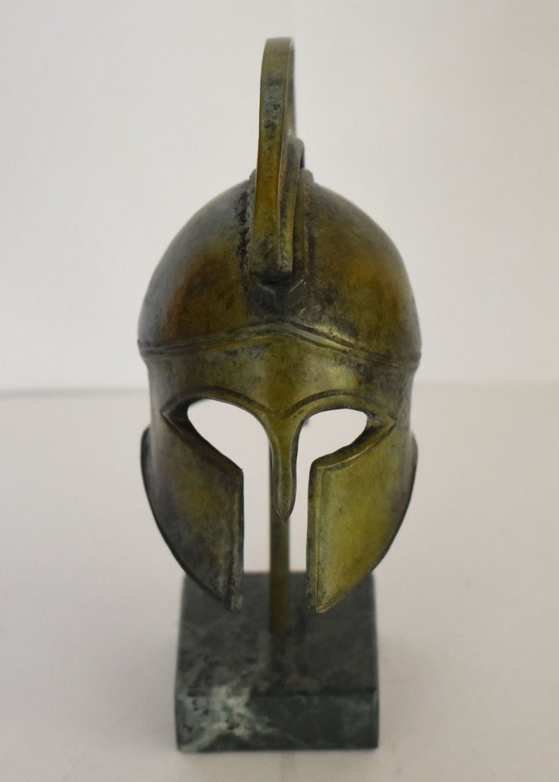May include: A bronze Greek warrior helmet with a plume on top, displayed on a black marble base.