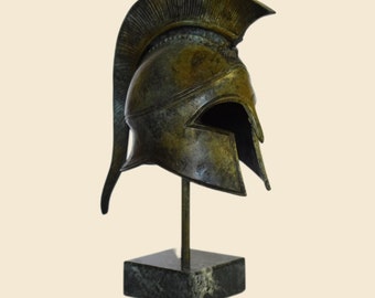 May include: A bronze replica of a Greek warrior helmet with a plume on top, displayed on a black marble base.