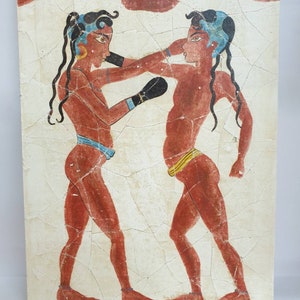 Op de afbeelding: Een schilderij dat twee figuren in een bokswedstrijd toont. De figuren zijn geschilderd in rood, blauw en geel op een witte achtergrond. De figuren dragen lendendoeken en hebben lang zwart haar. Het schilderij is op een rechthoekig doek.