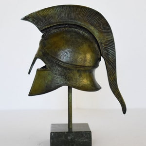 May include: A bronze replica of a Greek warrior helmet with a plume on a black marble base.