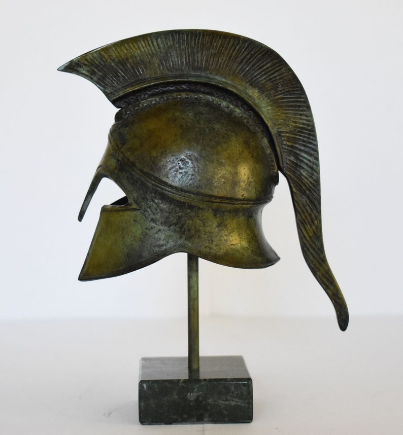 May include: A bronze replica of a Greek warrior helmet with a plume on a black marble base.