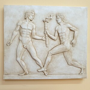 May include: A white plaster wall relief sculpture depicting two nude figures, one passing a torch to the other. The figures are in a classical style, with the torch bearer running and the other figure standing.