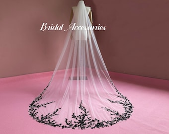 May include: A white bridal veil with a black floral lace trim. The veil is long and flowing, and the lace trim is delicate and intricate.
