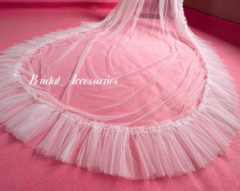 May include: White tulle bridal veil with a ruffled edge. The veil is laid out on a pink surface. The text "Bridal Accessories" is visible in the center of the veil.