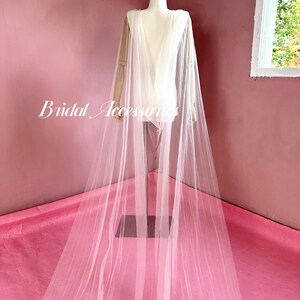 Pu&ograve; includere: Un velo da sposa in tulle bianco con un lungo strascico, drappeggiato su un manichino. Il velo &egrave; trasparente e delicato, con una texture morbida e fluida.