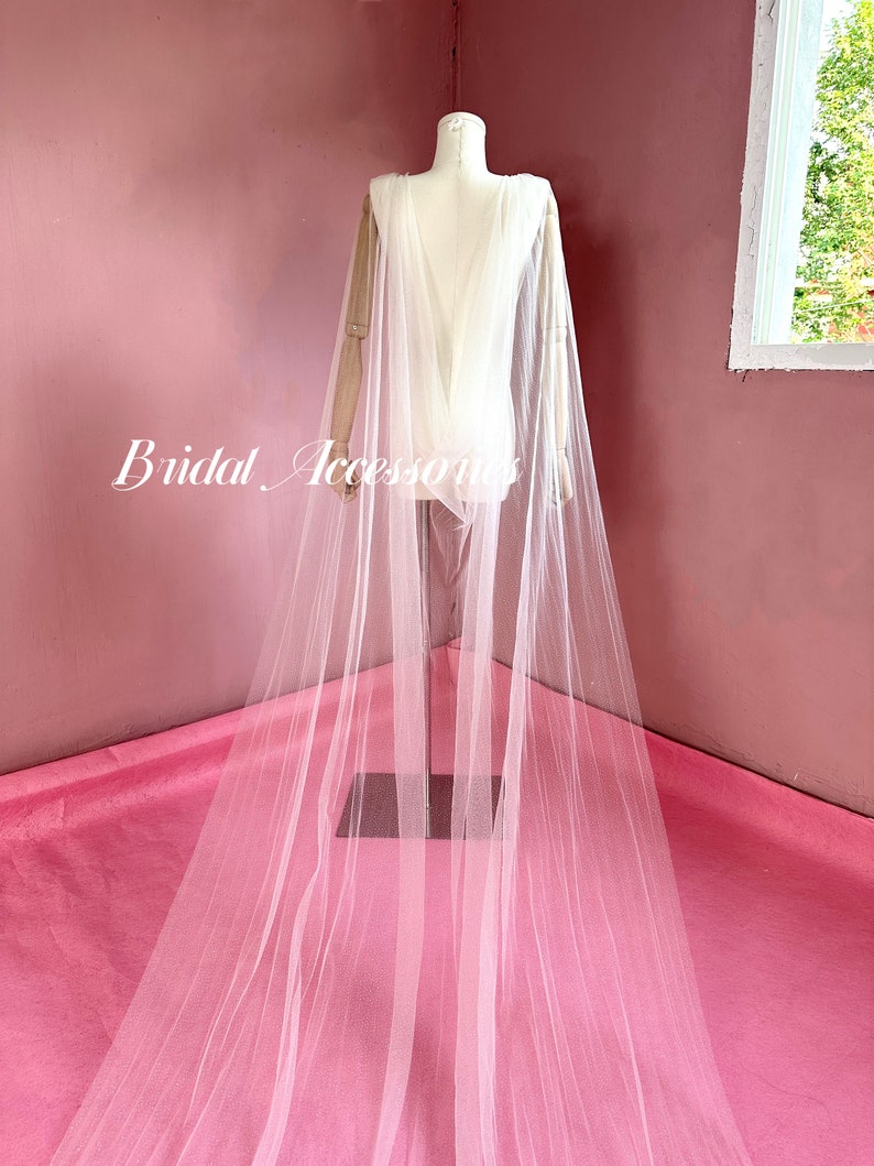Pu&ograve; includere: Un velo da sposa in tulle bianco con un lungo strascico, drappeggiato su un manichino. Il velo &egrave; trasparente e delicato, con una texture morbida e fluida.