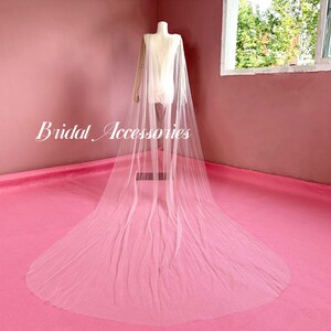Pu&ograve; includere: Un velo da sposa in tulle bianco con un lungo strascico, drappeggiato su un manichino. Il velo &egrave; realizzato in tessuto morbido e trasparente e ha un design delicato e fluido.