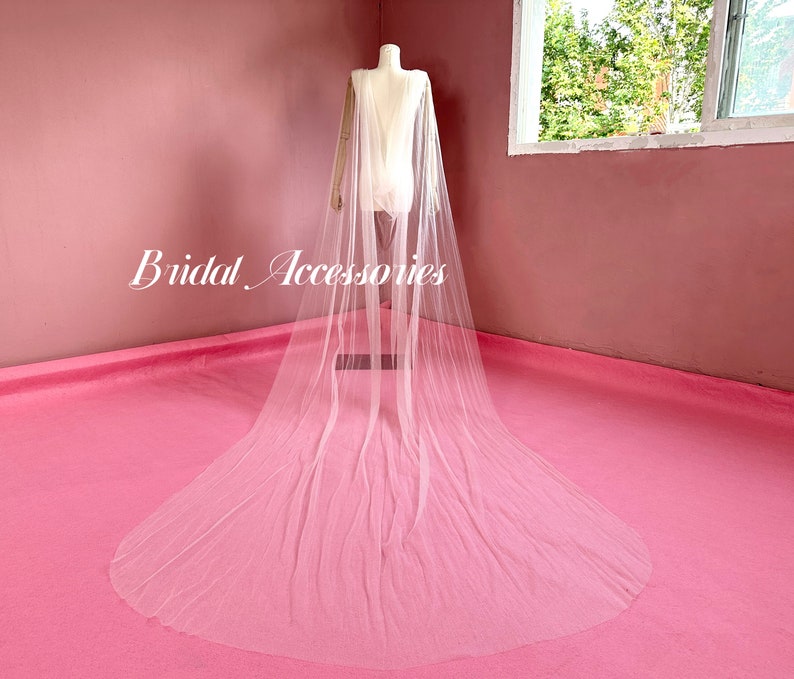 Pu&ograve; includere: Un velo da sposa in tulle bianco con un lungo strascico, drappeggiato su un manichino. Il velo &egrave; realizzato in tessuto morbido e trasparente e ha un design delicato e fluido.
