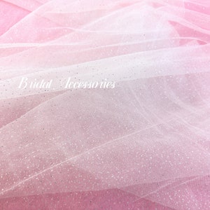 Pu&ograve; includere: Un primo piano di un tessuto di tulle bianco con un effetto ombr&eacute; rosa e glitter argentato. Il tessuto &egrave; morbido e delicato, perfetto per aggiungere un tocco di brillantezza a qualsiasi progetto.