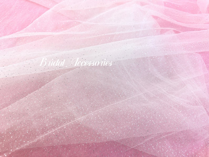 Pu&ograve; includere: Un primo piano di un tessuto di tulle bianco con un effetto ombr&eacute; rosa e glitter argentato. Il tessuto &egrave; morbido e delicato, perfetto per aggiungere un tocco di brillantezza a qualsiasi progetto.
