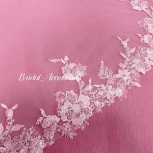 May include: A sheer white veil featuring an intricate floral lace border with delicate embroidery, small white beads, and shimmering sequins. The text "Bridal Accessories" is printed in white script on the left side of the lace pattern.
