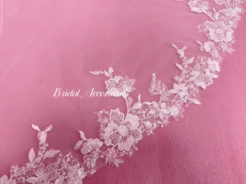 May include: A sheer white veil featuring an intricate floral lace border with delicate embroidery, small white beads, and shimmering sequins. The text "Bridal Accessories" is printed in white script on the left side of the lace pattern.