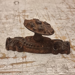Puede incluir: Manija de puerta antigua de bronce con un diseño floral decorativo. La manija presenta un pomo redondo y una base rectangular con bordes enrollados. El metal tiene una apariencia desgastada y envejecida, lo que sugiere que es vintage.