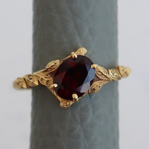 Peut inclure: Une bague en or avec une pierre précieuse rouge et des détails en forme de feuilles.