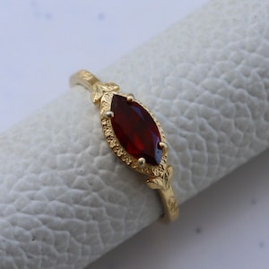 May include: A gold ring featuring a red marquise-shaped gemstone set in a delicate floral design.