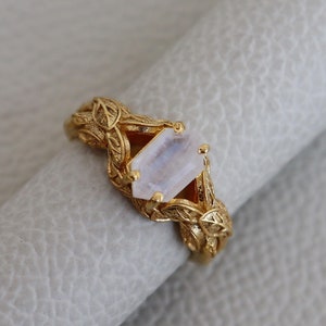 May include: A gold ring with a delicate leaf design and a clear, rectangular gemstone.