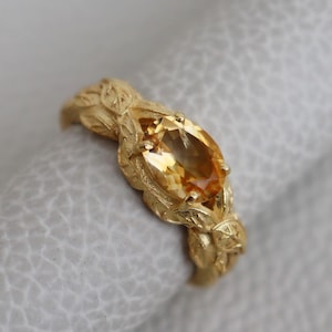 Peut inclure: Une bague en or avec un motif délicat de feuilles et une grande pierre précieuse de topaze de forme ovale.