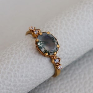 May include: A gold ring featuring a green moss agate oval stone with small diamond accents.