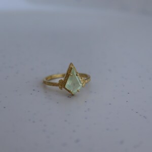 May include: A gold ring with a light green gemstone in a geometric shape.