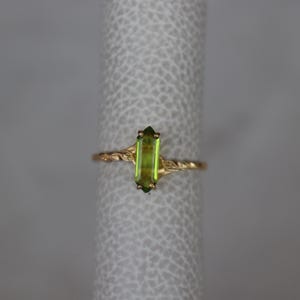 Pu&ograve; includere: Un anello d'oro con una pietra preziosa rettangolare verde chiaro. La fascia dell'anello presenta un delicato design a torsione con accenti di foglie. La gemma misura circa 1,3 cm di lunghezza.