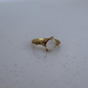 May include: A gold ring with a white moonstone set in a leaf design.