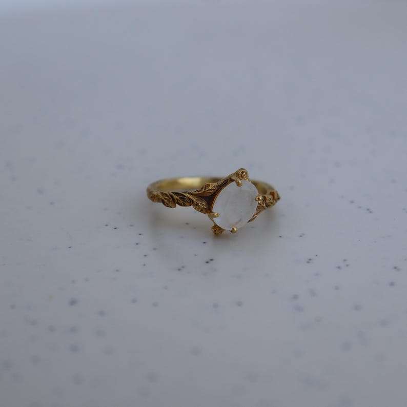May include: A gold ring with a white moonstone set in a leaf design.