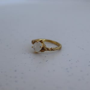 May include: A gold ring with a white moonstone set in a delicate, leafy design.