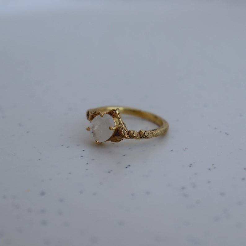 May include: A gold ring with a white moonstone set in a delicate, leafy design.