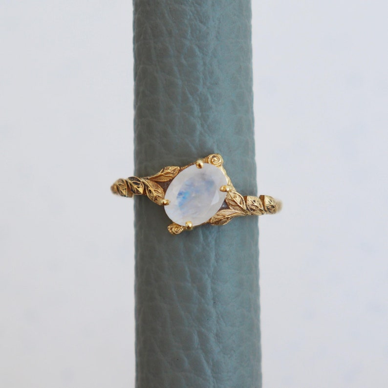 May include: A gold ring with a delicate leaf design and a white moonstone oval gemstone.