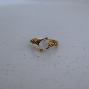 May include: A gold ring with a white oval gemstone set in a leaf design.