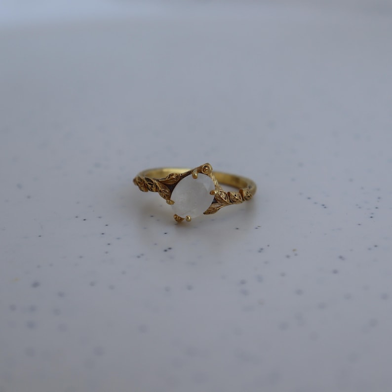 May include: A gold ring with a white oval gemstone set in a leaf design.