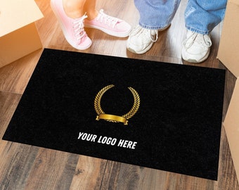 Puede incluir: Alfombra de bienvenida negra con una corona de laurel dorada y el texto "YOUR LOGO HERE" en blanco. Dos personas están de pie sobre la alfombra.