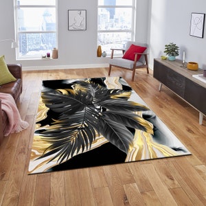 May include: A black and gold area rug with a tropical leaf design. The leaves are black with gold accents and are set against a white background with gold and black marble swirls.