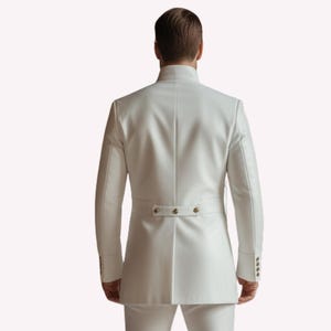 Puede incluir: Chaqueta de traje blanca con cuello mandar&iacute;n y detalles de botones. La chaqueta tiene mangas largas y un corte entallado. La parte trasera de la chaqueta presenta un peque&ntilde;o detalle de cintur&oacute;n con tres botones. El traje es de color blanco liso.