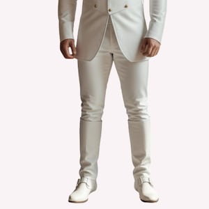 Puede incluir: Un traje blanco con una chaqueta cruzada y pantalones a juego. El conjunto incluye botas blancas con hebilla. La chaqueta tiene botones dorados. El traje est&aacute; hecho de un material liso, posiblemente similar al cuero.