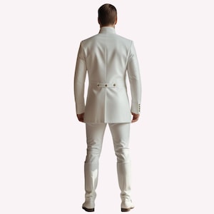 Puede incluir: Un traje blanco, que incluye una chaqueta de cuello alto con botones decorativos y pantalones a juego. El atuendo se completa con botas blancas. La persona se ve desde atr&aacute;s, mostrando el ajuste y el dise&ntilde;o del traje.