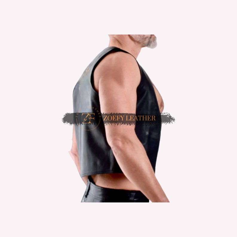 May include: A black leather vest with a sleeveless design. The vest has a cropped length and is made of a smooth, supple leather. The vest is shown on a model, with the text "ZOE FY LEATHER" visible on the front.