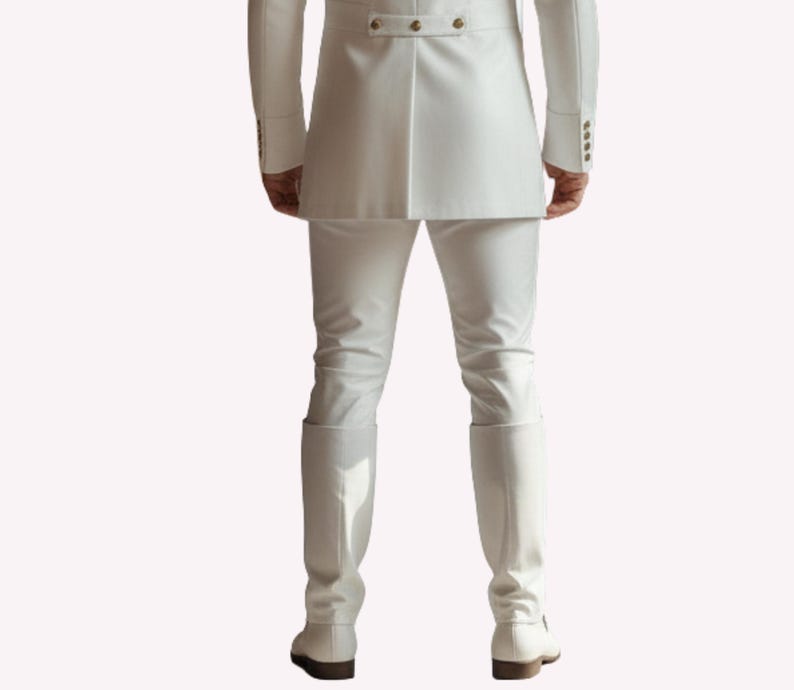 Puede incluir: Un traje blanco, que incluye una chaqueta con botones dorados, pantalones y botas. El conjunto es de color blanco brillante. Las botas altas hasta la rodilla tienen un peque&ntilde;o tac&oacute;n. El atuendo es formal.