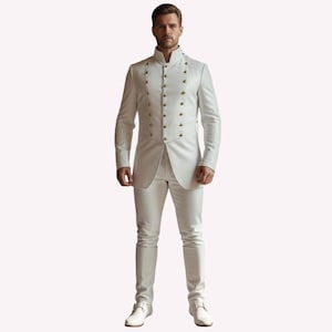 Puede incluir: Un traje blanco con cuello alto y botones dorados. La chaqueta tiene un dise&ntilde;o cruzado y mangas largas. Los pantalones son ajustados y las botas son blancas. El traje es de estilo formal.