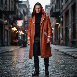May include: A long, rust-colored hooded coat featuring silver metallic trim along the front opening, cuffs, and pocket flaps. The coat is worn over a black turtleneck sweater and black trousers, paired with dark brown leather lace-up boots.