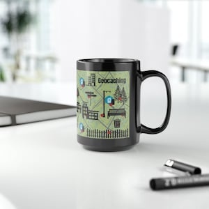 Puede incluir: Taza de café negra con un diseño blanco de un mapa con la palabra "Geocaching" impresa en ella.