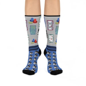 May include: A pair of blue and gray socks with a pattern of hockey and air hockey tables and pucks. The socks have a black and white pattern on the bottom.